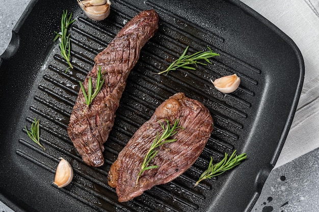 Geroosterd op een grillpan Flank flap of Bavette beef steak met rozemarijn Grijze achtergrond Bovenaanzicht