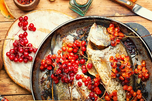 Geroosterde dorado-vis in een pan met herfstviburnumbessen. Huisgemaakt herfstrecept
