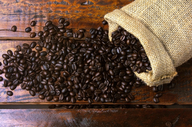 Geroosterde en verse koffiebonen in rustieke stoffen tas en gegoten over rustieke houten tafel. Bovenaanzicht