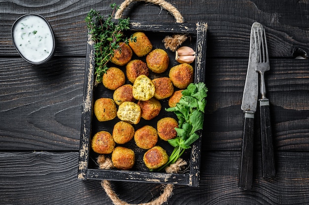 Geroosterde falafelballetjes van kikkererwten met knoflookyoghurtsaus in een houten bakje.