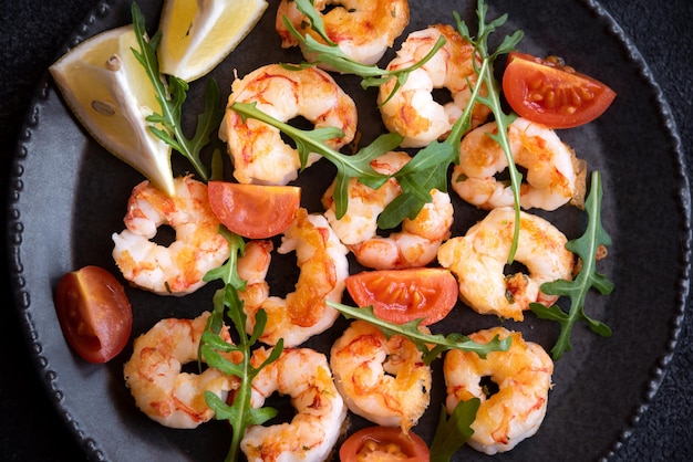 Foto geroosterde garnalen met tomaten en rucola op zwarte plaat