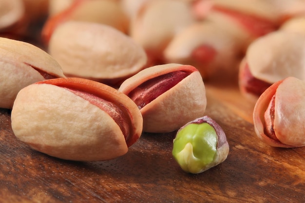 Geroosterde gezouten Turkse rode pistachenoten, een van hen gepeld, groen zaad zichtbaar, op een houten bord. Close-updetail.