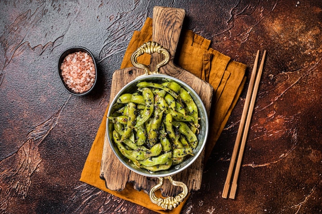 Geroosterde groene Edamame sojabonen met zeezout en sesamzaadjes in een koekenpan Donkere achtergrond Bovenaanzicht