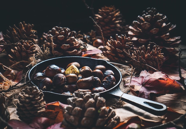 Geroosterde kastanjes in een kleine ijzeren pan op een tafel met herfstbladeren en dennenappels