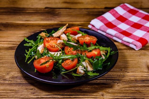 Geroosterde kipfilet en salade met rucola en cherrytomaatjes in een zwart bord