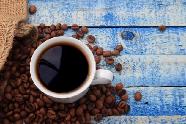 Geroosterde koffiebonen en een glas warme koffie op een blauw houten bord met kopieerruimte