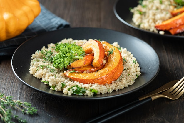 Geroosterde pompoensalade met quinoa boerenkool en pijnboompitten in een zwarte plaat op houten ondergrond