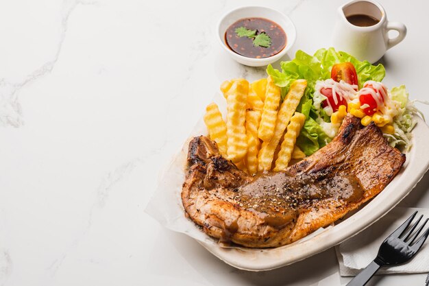 Geroosterde pork chop steak met salade en pikante saus op witte tafel achtergrond