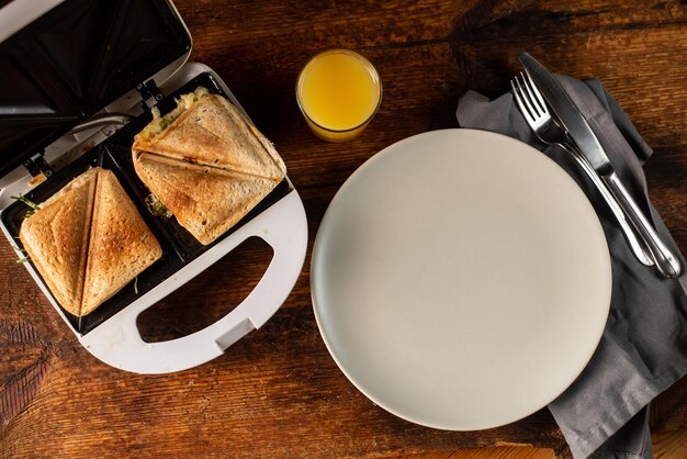 Geroosterde sandwiches op een toastsandwich een leeg bord en een glas jus d'orange op een houten achtergrond Lichte ochtendontbijtsnack