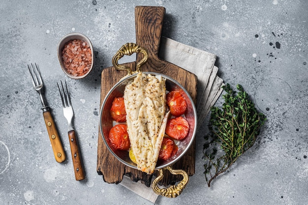 Geroosterde Schelvisfilet in koekenpan met tomaat en aardappel. Grijze achtergrond. Bovenaanzicht.