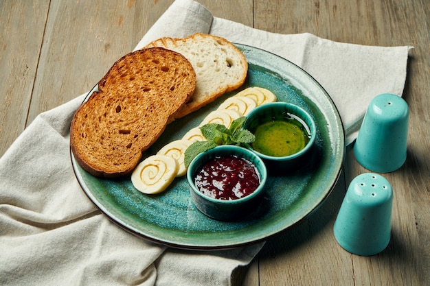 Geroosterde sneetjes brood met gekruide boter, jam en honing op een turquoise plaat op een houten oppervlak. continentaal ontbijt. close up bekijken