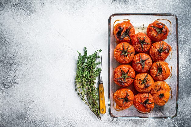 Geroosterde tomaten met olijfolie en tijm in ovenschaal. witte achtergrond. bovenaanzicht. ruimte kopiëren.