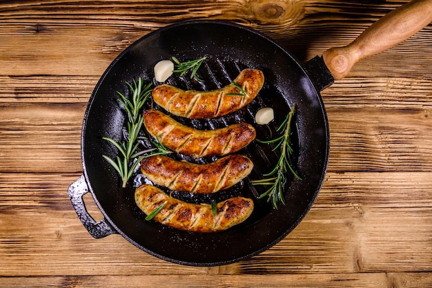 Geroosterde worstjes met rozemarijntakjes en knoflook in een gietijzeren grillpan Bovenaanzicht