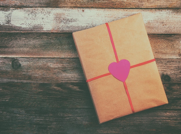 Foto geschenk voor de valentijnsdag verpakkingspapier gebonden met een rood lint met een hart op houten vintage grunge achtergrond met ruimte voor tekst bovenaan close-up getinte foto