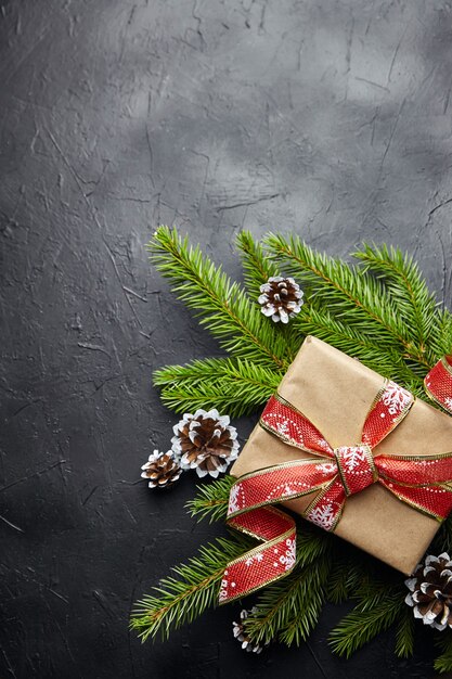 Geschenkdoos en groene kerstboomtak met kegel op zwarte achtergrond bovenaanzicht