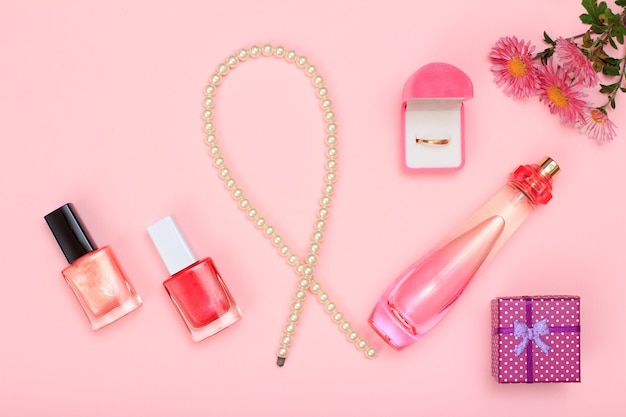Geschenkdoos, kralen, fles parfum, nagellak en gouden ring in doos op een roze achtergrond. Vrouwen cosmetica en accessoires. Bovenaanzicht.