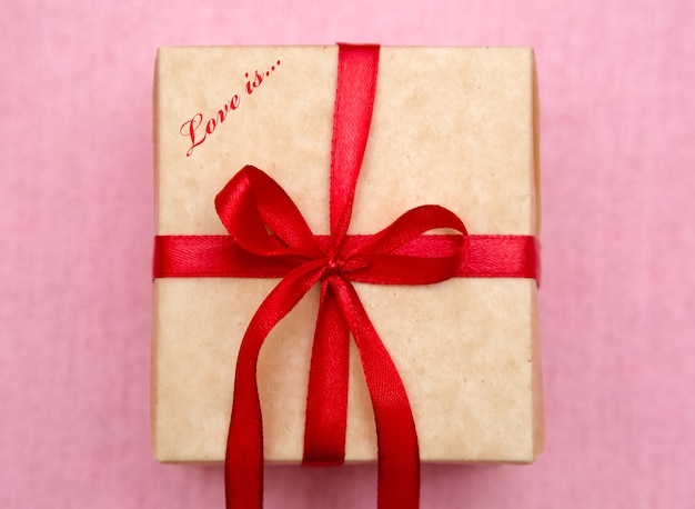 Geschenkdoos met een rode strik op een roze achtergrond. Cadeau voor geliefden