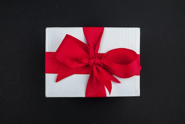Geschenkdoos met een rood lint op een zwarte ondergrond Witte doos met rode strik