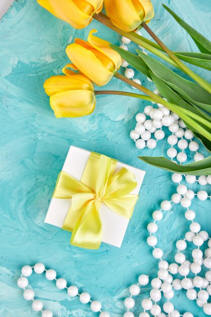 Geschenkdoos met geel lint in de buurt van tulpenbloemen en ketting