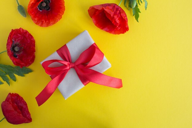 Geschenkdoos met rood lint en rode papavers op het gele oppervlak. bovenaanzicht. kopieer ruimte.