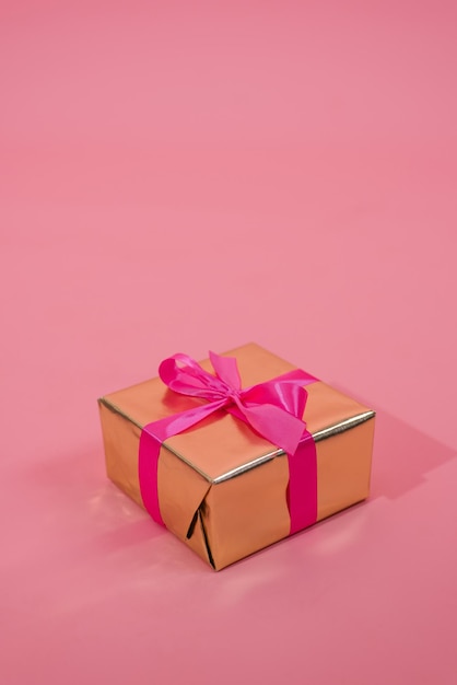 Geschenkdoos op roze achtergrond een geschenk in goudpapier versierd met een stijlvolle elegante fuchsia satijnen strik het concept van kerstmis en andere feestdagen