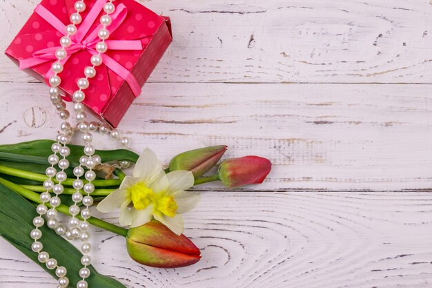 Geschenkdoos parelhalsband en boeket van rode tulpen en narcissen op houten achtergrond Concept van Valentijnsdag Vrouwendag Moederdag en verjaardag Bovenaanzicht kopie ruimte