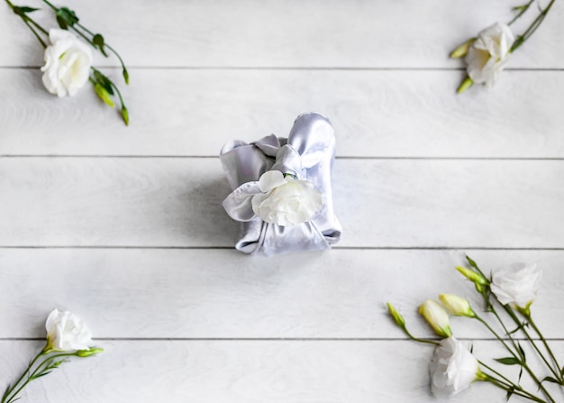 Geschenkdoos trendy verpakt in zijde stof in Furoshiki techniek witte bloemen Eustoma of Lisianthu op lichte houten achtergrond