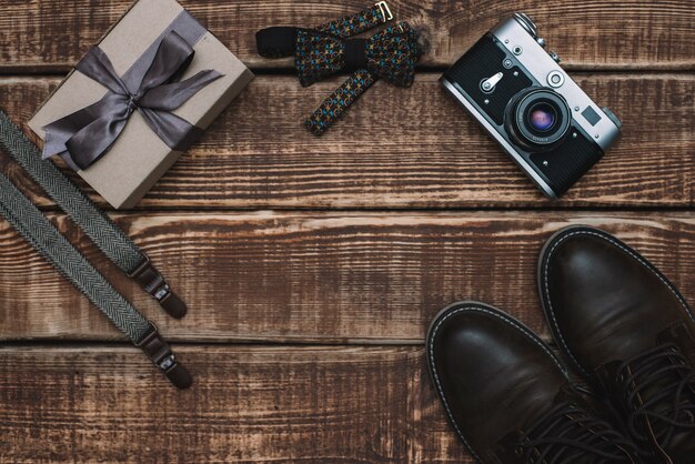 Geschenkdoos voor vaderdag met herenaccessoires vlinderdas, retro camera, bretels en leren schoenen op een houten tafel. plat liggen.