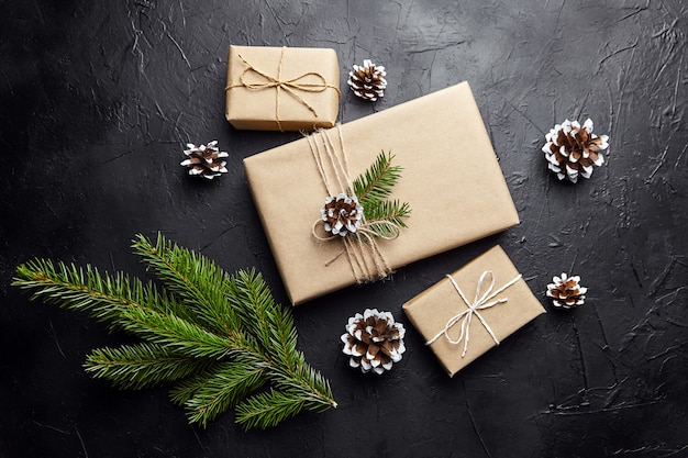 Geschenkdozen en groene kerstboomtak met kegel op donkere achtergrond bovenaanzicht