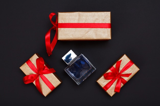 Geschenkdozen gebonden met rode linten en fles parfum op zwarte achtergrond. Wenskaart concept. Bovenaanzicht.