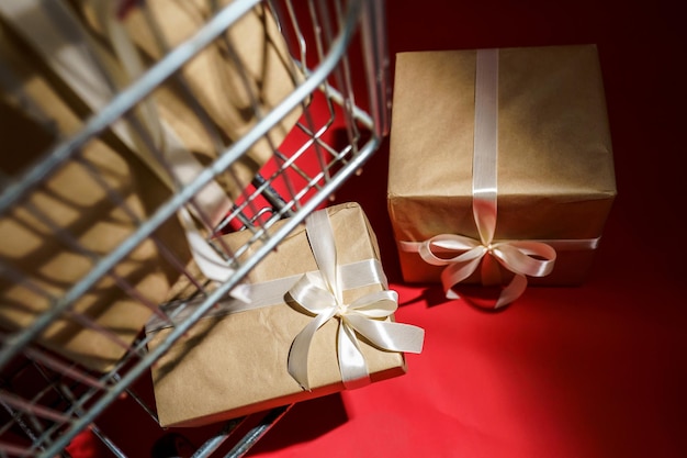 Geschenken in ambachtelijk papier met witte tape in een supermarktkarretje op een rode achtergrond