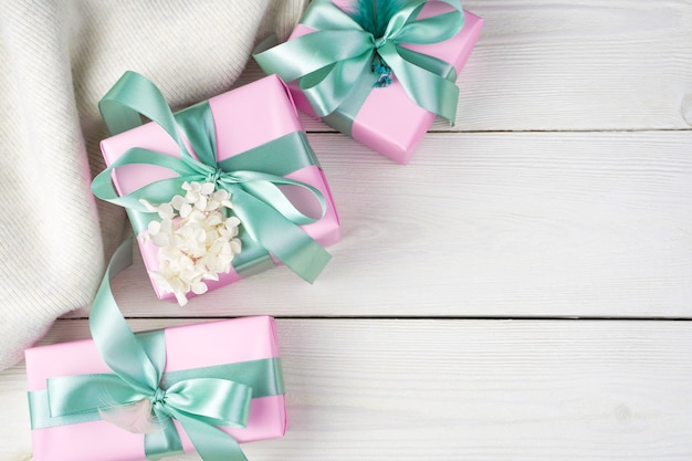 Geschenken in roze verpakking met linten en een trui op een witte houten achtergrond.