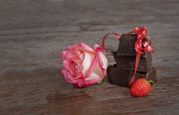 Geschenkset bloem, chocolade en aardbei. rose en stukjes chocolade met bessen op een houten achtergrond.