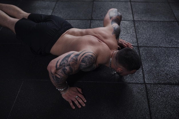 Gescheurde getatoeëerde sportman die push-ups doet in de sportschool