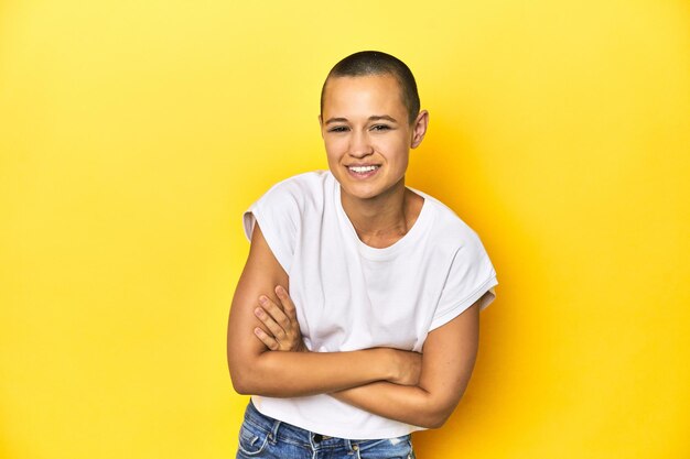 Gescheurde vrouw in een witte tanktop met een gele achtergrond die lacht en plezier heeft.