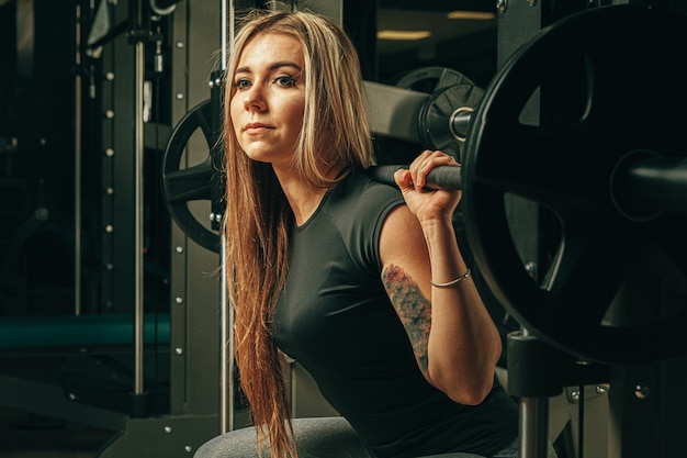 Geschikte vrouw die hurkzit in een machine van Smith in gymnastiek doen