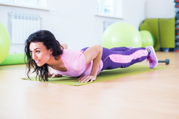 Geschikte vrouw die plankoefening en opdrukoefeningen doen die aan triceps van buikspieren werken.