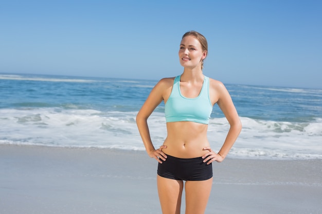 Geschikte vrouw die zich op het strand met handen op heupen op een zonnige dag bevindt