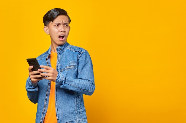 Geschokt Aziatische jongeman die naar bericht op smartphone kijkt