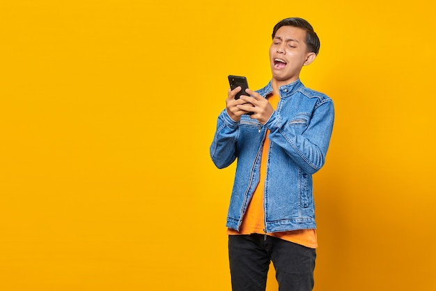 Geschokt Aziatische jongeman die naar bericht op smartphone kijkt