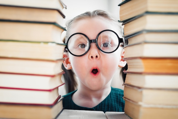 Foto geschokt blond meisje van 46 jaar oud met een bril toont tong in bibliotheek tussen veel boeken