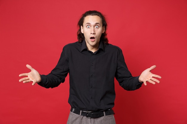 Geschokt boos stijlvolle jonge krullend langharige man in zwart shirt poseren geïsoleerd op rode muur achtergrond studio portret. mensen oprechte emoties levensstijl concept. bespotten kopie ruimte. camera kijken.