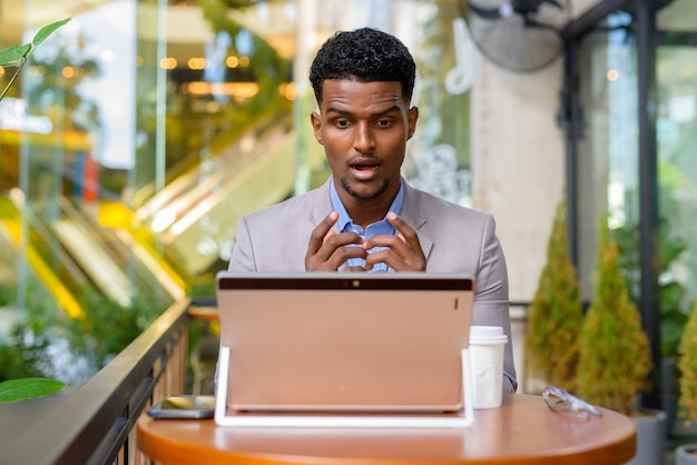 Geschokt en verrast Afrikaanse zakenman bij coffeeshop met behulp van laptopcomputer