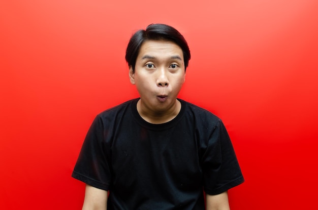 Geschokt gezicht van Aziatische man in zwart shirt op rode achtergrond