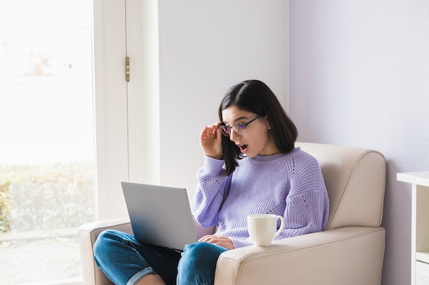 Geschokt jonge etniciteit vrouw op zoek in computer en vaststelling van haar bril. lockdown nieuws, online schokkend lage prijs.