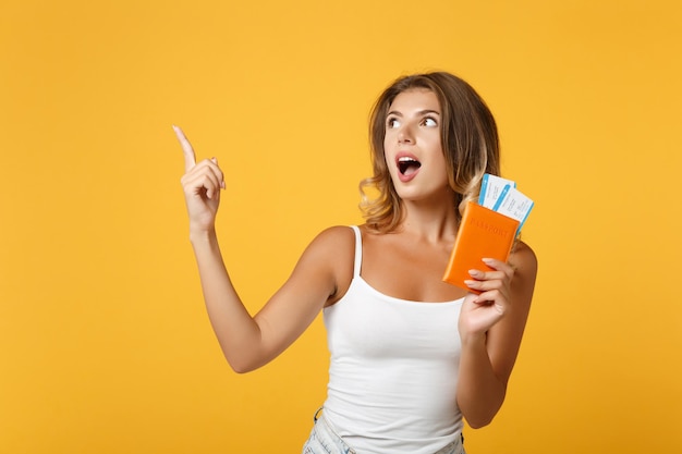 Geschokt jonge vrouw meisje in lichte casual kleding poseren geïsoleerd op geel oranje achtergrond. Mensen levensstijl concept. Bespotten kopie ruimte. Wijs wijsvinger omhoog, houd paspoort, instapkaart, ticket vast.