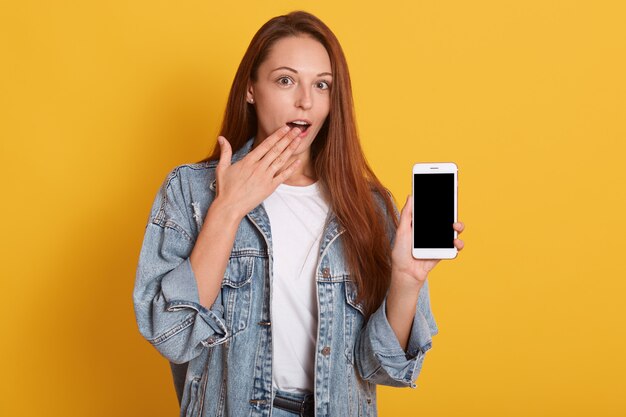 Geschokt Kaukasisch meisje dat met wijsvinger op het lege scherm van mobiele telefoon richt