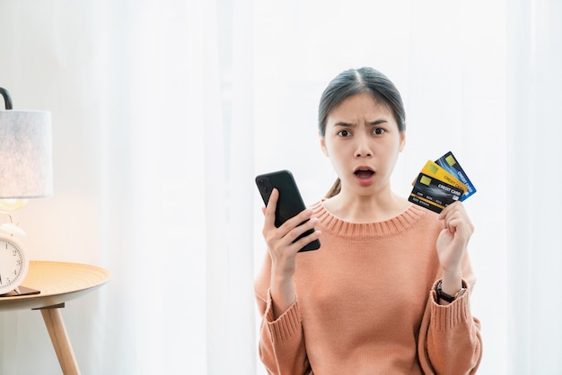 Geschokt opgewonden Aziatische vrouw met creditcard en smartphone, omdat veel uitgaven.