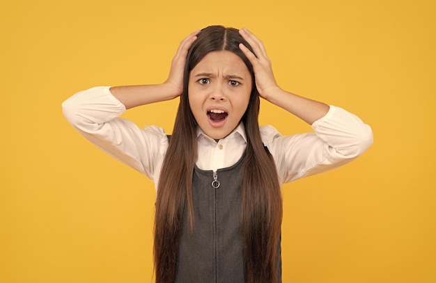 Geschokt tienermeisje in schooluniform neemt hoofd in handen gele achtergrond schok