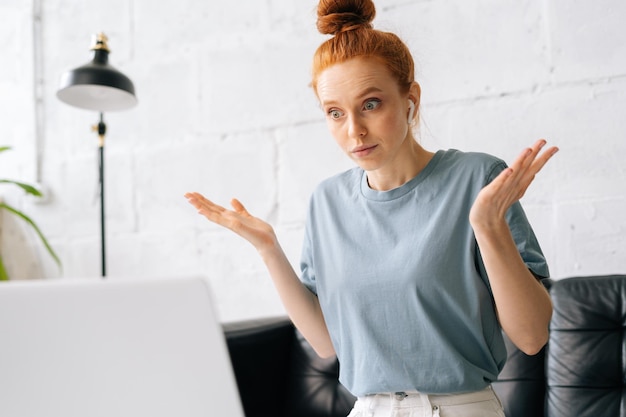 Geschokt verrast mooie roodharige jonge vrouw kijkt op het scherm van de laptopcomputer. Gestresst gefrustreerd meisje spreekt op videogesprek met vriendcliëntcollega.